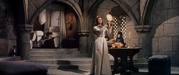 Movie still from “El Cid” (1961), directed by Anthony Mann – A woman in a white dress holding a mirror in front of a table; Wide shot, Low angle