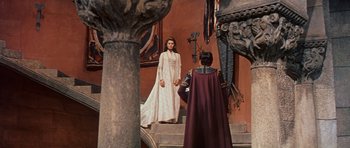 Movie still from “El Cid” (1961), directed by Anthony Mann – A woman in a white dress standing next to a man in a red cape; Wide shot, Over the shoulder angle