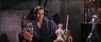 Movie still from “El Cid” (1961), directed by Anthony Mann – A man holding a wine glass sitting on a table; Medium shot, Low angle