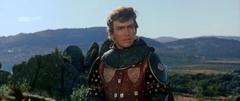 Movie still from “El Cid” (1961), directed by Anthony Mann – A man in a medieval outfit standing in front of a mountain; Close Up shot, Over the shoulder angle