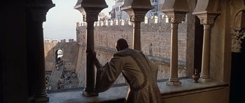 Movie still from “El Cid” (1961), directed by Anthony Mann – A man leaning on a pillar on the side of a building; Wide shot, High angle
