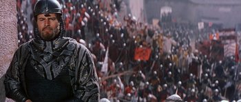 Movie still from “El Cid” (1961), directed by Anthony Mann – A large crowd of people in helmets marching down a street; Medium shot, Over the shoulder angle