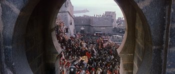Movie still from “El Cid” (1961), directed by Anthony Mann – A large crowd of people gathered in front of a stone wall; Extreme Wide shot, High angle