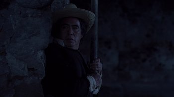Movie still from “El Norte” (1983), directed by Gregory Nava – A man holding a stick in a dark room; Medium shot, Low angle