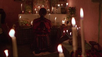 Movie still from “El Norte” (1983), directed by Gregory Nava – A woman kneeling in front of a group of lit candles; Medium shot, High angle