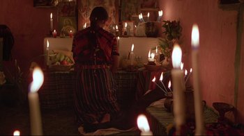 Movie still from “El Norte” (1983), directed by Gregory Nava – A woman is standing in front of candles in a room; Medium shot, Low angle