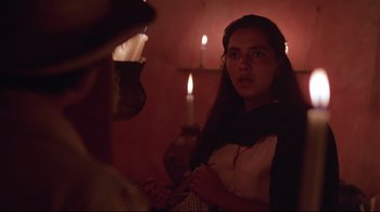 Movie still from “El Norte” (1983), directed by Gregory Nava – A woman standing in a room with candles in the background; Close Up shot, Over the shoulder angle