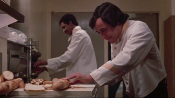 Movie still from “El Norte” (1983), directed by Gregory Nava – A man in a chef's outfit making bread in front of another man; Medium shot, Low angle