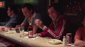 Movie still from “El Norte” (1983), directed by Gregory Nava – Two men sitting at a table with a bottle of beer; Medium shot, Over the shoulder angle