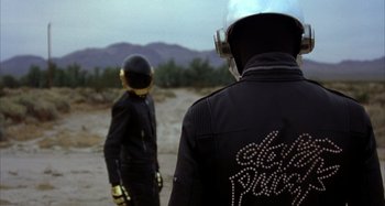 Two people in black jackets standing on a dirt field