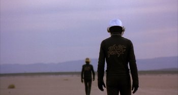 Two people in wetsuits walking on the beach