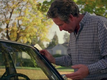 Movie still from “Elephant” (2003), directed by Gus Van Sant – A man looking through a car window in a yard; Medium shot, Over the shoulder angle