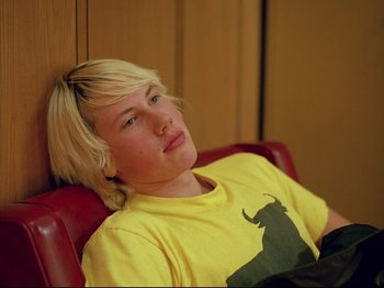 Movie still from “Elephant” (2003), directed by Gus Van Sant – A person sitting in a chair wearing a yellow t - shirt; Close Up shot, Low angle