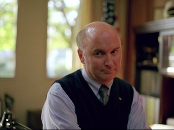 Movie still from “Elephant” (2003), directed by Gus Van Sant – A man with a bald head wearing a vest and tie; Close Up shot, High angle