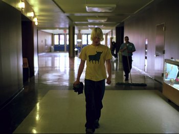 Movie still from “Elephant” (2003), directed by Gus Van Sant – A man walking down a hall way with a camera; Wide shot, Low angle