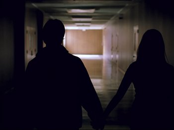 Movie still from “Elephant” (2003), directed by Gus Van Sant – A man and a woman holding hands in a dark hallway; Medium shot, Low angle