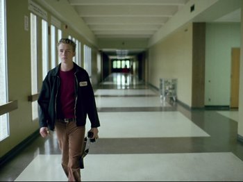 Movie still from “Elephant” (2003), directed by Gus Van Sant – A young man walking down a hallway holding a camera; Wide shot, Low angle