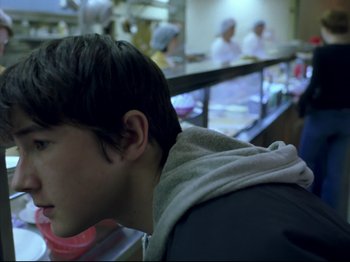 Movie still from “Elephant” (2003), directed by Gus Van Sant – A young man sitting in front of a counter in a kitchen; Close Up shot, Over the shoulder angle