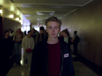 Movie still from “Elephant” (2003), directed by Gus Van Sant – A young man standing in a hallway with a crowd of onlookers behind him; Close Up shot, Low angle