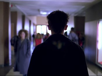 Movie still from “Elephant” (2003), directed by Gus Van Sant – A man standing in a hallway with people in the background; Medium shot, Over the shoulder angle