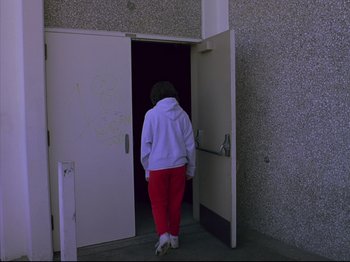 Movie still from “Elephant” (2003), directed by Gus Van Sant – A person in a white hoodie walking through a door way; Wide shot, Low angle