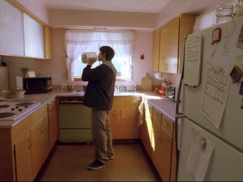 Movie still from “Elephant” (2003), directed by Gus Van Sant – A man drinking a cup of coffee in a kitchen; Wide shot, High angle