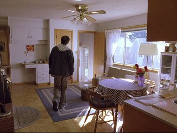 Movie still from “Elephant” (2003), directed by Gus Van Sant – A man standing in a room looking out the window; Wide shot, High angle
