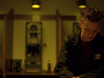 Movie still from “Elephant” (2003), directed by Gus Van Sant – A man in a black jacket is looking down at a book; Medium shot, Low angle