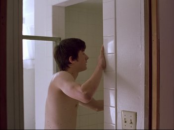 Movie still from “Elephant” (2003), directed by Gus Van Sant – A young man in a bathroom touching a wall; Medium shot, Over the shoulder angle