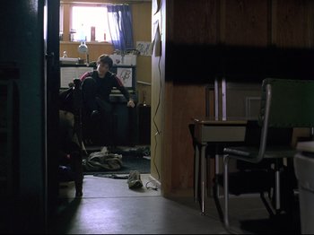 Movie still from “Elephant” (2003), directed by Gus Van Sant – A person sitting on a chair in a room; Wide shot, High angle