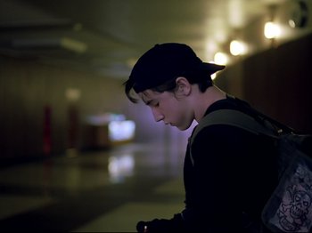 Movie still from “Elephant” (2003), directed by Gus Van Sant – A young man looking at his cell phone in the dark; Medium shot, Low angle