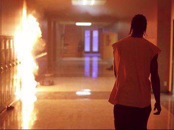 Movie still from “Elephant” (2003), directed by Gus Van Sant – A person standing in a hallway with a fire coming out of it; Wide shot, Low angle