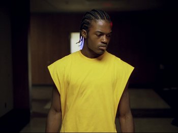 Movie still from “Elephant” (2003), directed by Gus Van Sant – A man in a yellow t - shirt is standing in a room; Medium shot, Low angle