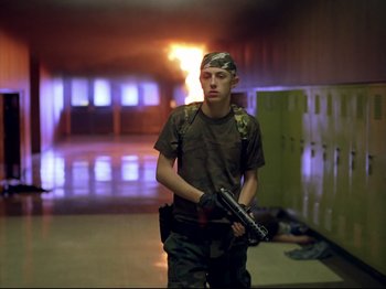 Movie still from “Elephant” (2003), directed by Gus Van Sant – A young man holding a gun in a hallway; Wide shot, Low angle