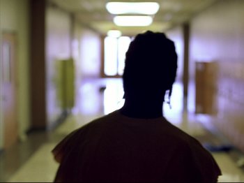 Movie still from “Elephant” (2003), directed by Gus Van Sant – A person standing in a hallway with a light shining on them; Medium shot, Low angle