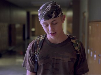 Movie still from “Elephant” (2003), directed by Gus Van Sant – A young man wearing a camouflage hat and a backpack; Close Up shot, Over the shoulder angle
