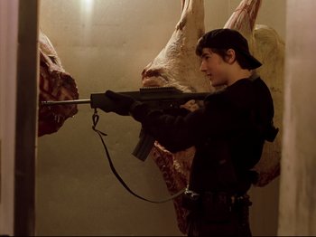 Movie still from “Elephant” (2003), directed by Gus Van Sant – A man holding a gun in front of a bunch of meat; Medium shot, Low angle