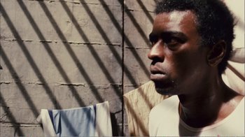 Movie still from “Elite Squad 2: The Enemy Within” (2010), directed by José Padilha – A young man sitting in front of a brick wall; Close Up shot, High angle