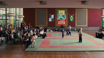 Movie still from “Elite Squad 2: The Enemy Within” (2010), directed by José Padilha – A group of people in a room watching a person kick a ball on the ground; Extreme Wide shot, High angle