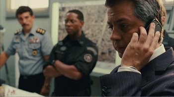 Movie still from “Elite Squad 2: The Enemy Within” (2010), directed by José Padilha – A man in a suit is on a cell phone while another man in a suit looks on; Close Up shot, Over the shoulder angle