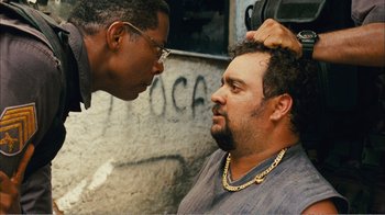 Movie still from “Elite Squad 2: The Enemy Within” (2010), directed by José Padilha – A man with a chain around his neck talking to another man; Close Up shot, Over the shoulder angle