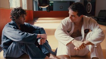 Movie still from “Elite Squad 2: The Enemy Within” (2010), directed by José Padilha – Two men sitting on the ground in a room; Medium shot, Over the shoulder angle