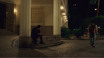 Movie still from “Elite Squad 2: The Enemy Within” (2010), directed by José Padilha – A man sitting on the steps of a building at night looking at his cell phone; Wide shot, Low angle