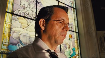 Movie still from “Elite Squad 2: The Enemy Within” (2010), directed by José Padilha – A person wearing glasses near a stained glass window; Close Up shot, Low angle