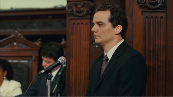 Movie still from “Elite Squad 2: The Enemy Within” (2010), directed by José Padilha – A man wearing a suit and tie standing in front of a microphone; Close Up shot, Over the shoulder angle