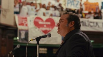 Movie still from “Elite Squad 2: The Enemy Within” (2010), directed by José Padilha – A man in a black jacket is speaking into a microphone; Medium shot, Low angle