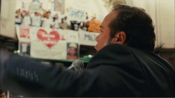 Movie still from “Elite Squad 2: The Enemy Within” (2010), directed by José Padilha – A man with a microphone sitting in front of a crowd of people; Close Up shot, Over the shoulder angle