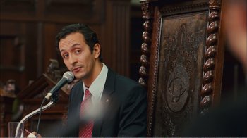 Movie still from “Elite Squad 2: The Enemy Within” (2010), directed by José Padilha – A man wearing a suit and tie while speaking into a microphone; Medium shot, Over the shoulder angle
