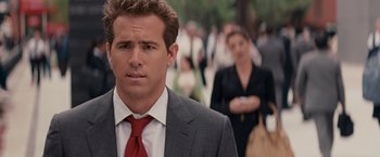 Movie still from “The Proposal” (2009), directed by Anne Fletcher – A man in a suit and red tie standing in front of a crowd of onlookers; Close Up shot, Over the shoulder angle