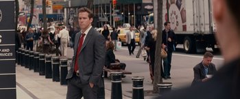 Movie still from “The Proposal” (2009), directed by Anne Fletcher – A man in a suit and tie standing on the sidewalk; Medium shot, Over the shoulder angle